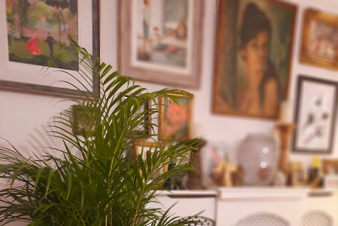 Focussed leafy houseplants with a blurred background showing a variety of framed wall art hung above a fireplace