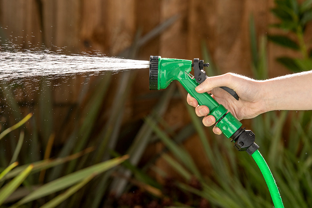 A person holding a garden hose, spraying water, and watering plants