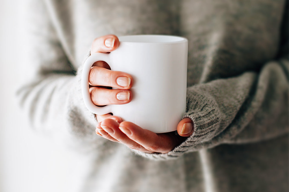 Person in a grey jumper holding a white mug with both hands