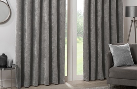 Hamilton McBride thick grey curtains hung on a living room window with a grey armchair in the foreground