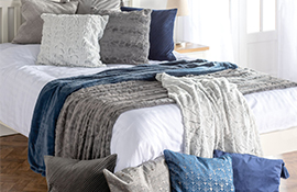 Hamilton McBride blue and grey throws and cushions scattered across a white double bed