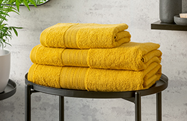 Hamilton McBride ochre yellow towels folded and stacked on a black metal table in a bathroo