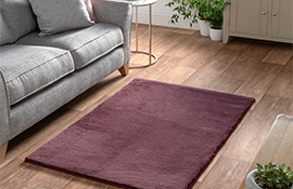 Hamilton McBride maroon cosy rug laying on a light wood floor in a living room with a light grey sofa